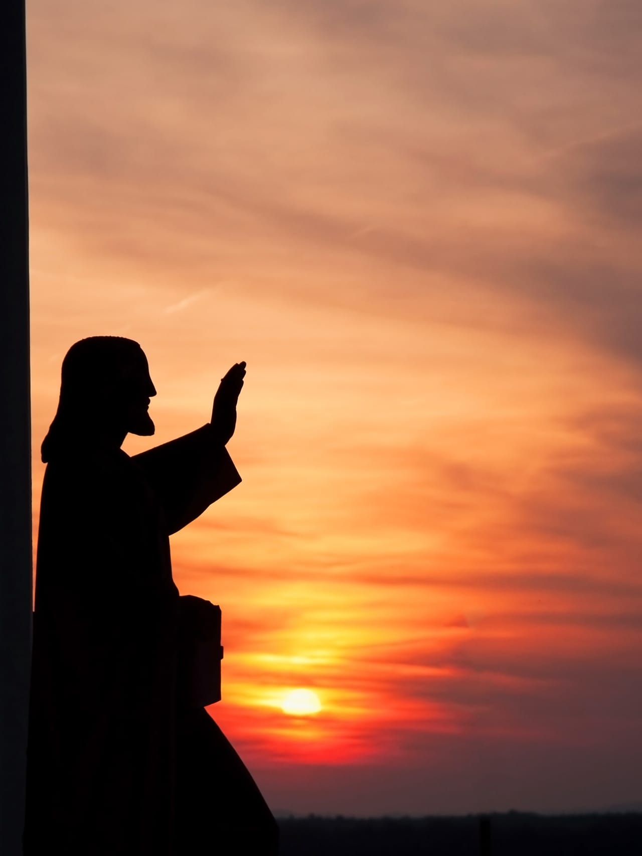 A statue of Christ with hand raised, silhouetted against a sunset sky