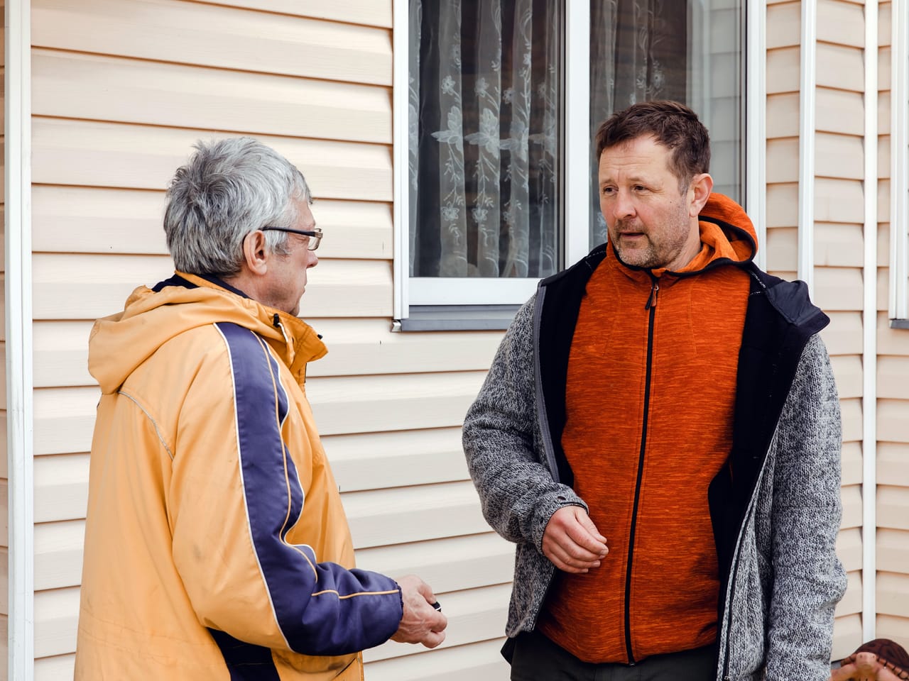 Two neighbors talking outside a house on an ordinary day