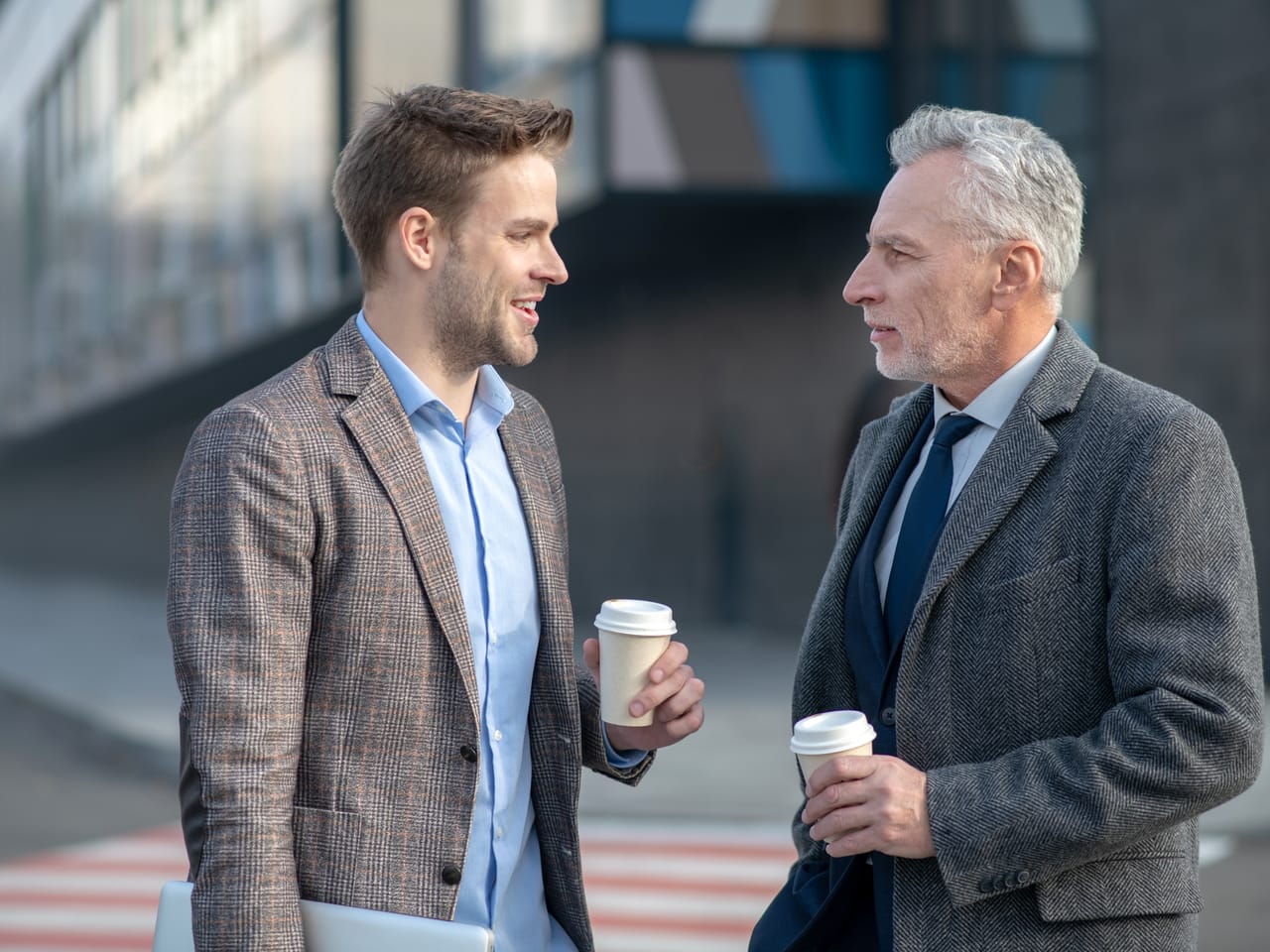 A younger and an older leader talking with coffee on a city street